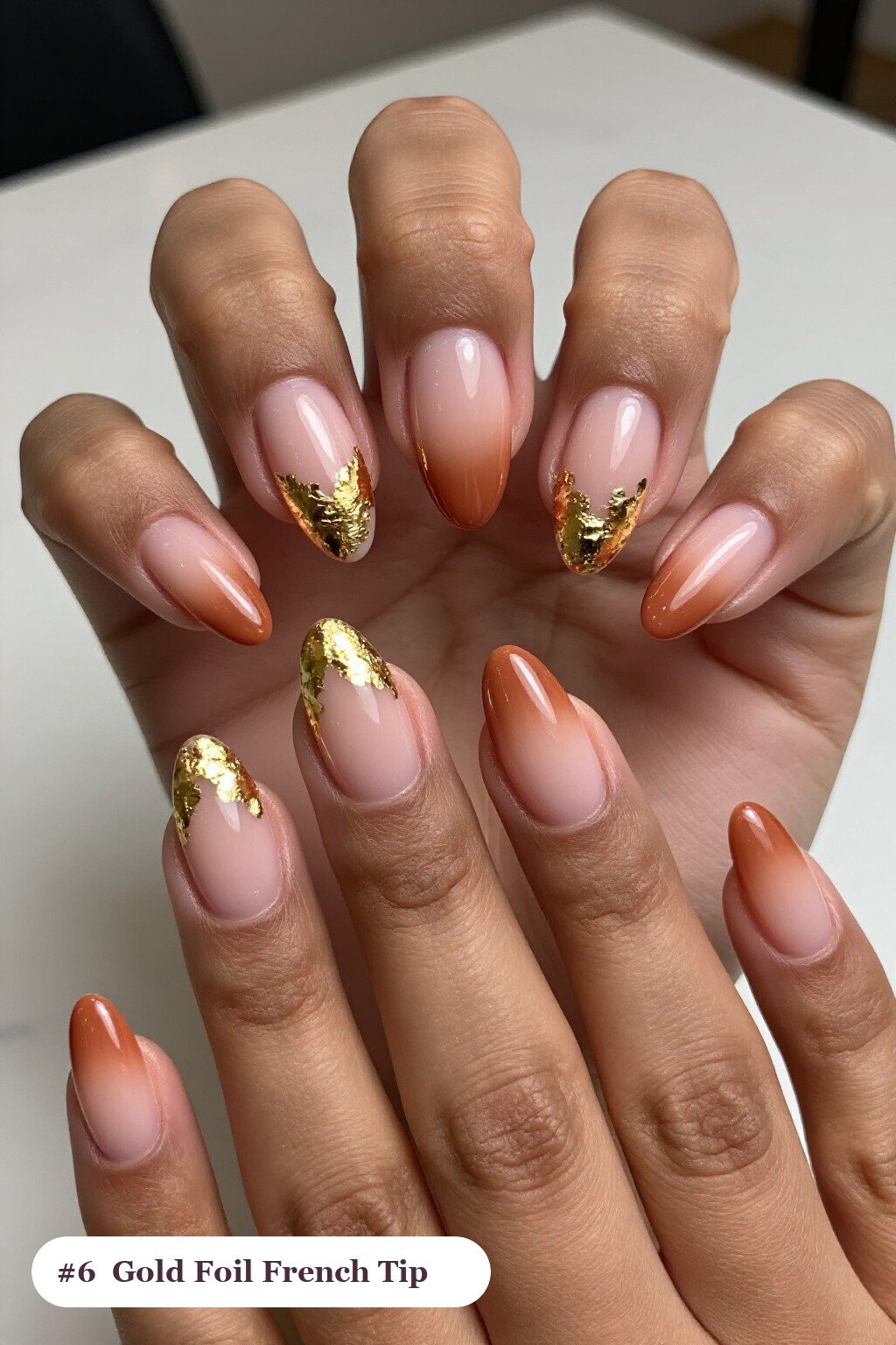 Medium almond terracotta ombre french nails with crisp french tips and a smooth ombre gradient clearly visible on every nail, styled with dense gold foil flakes and gold leaf scattered across every nail - ombre french almond nails