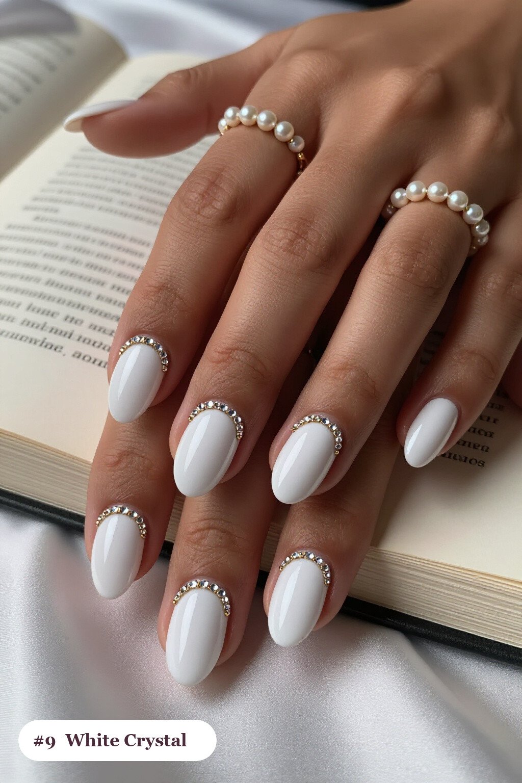 Medium oval white nails with rows of sparkling crystal rhinestones along the cuticle of every nail, with gold details, perfect for winter - winter white nails